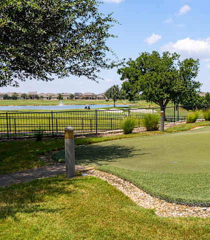 A golf course with a green and a small pond in the background.