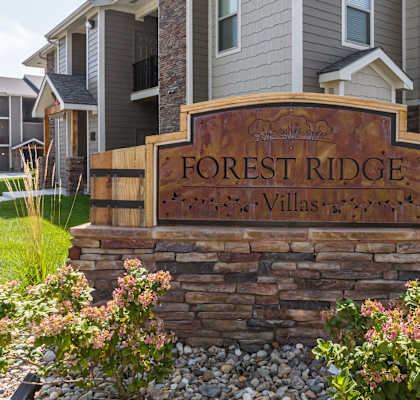 A sign that says Forest Ridge Villas in front of some houses.