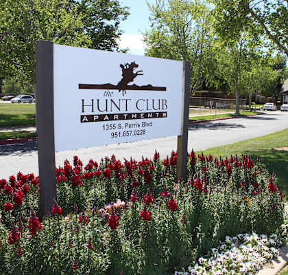 A sign for The Hunt Club Apartments stands in front of a flower bed.