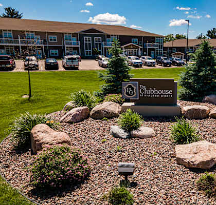 A landscaped area with a sign that says "Clubhouse" in front of a building.
