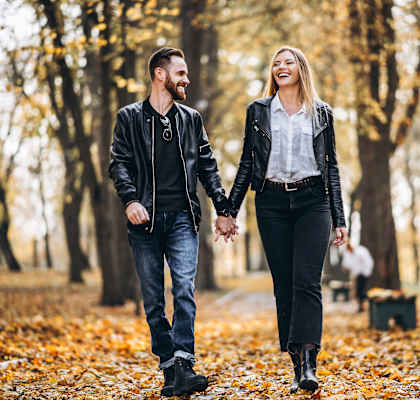 A couple walking hand in hand through a park in autumn.
