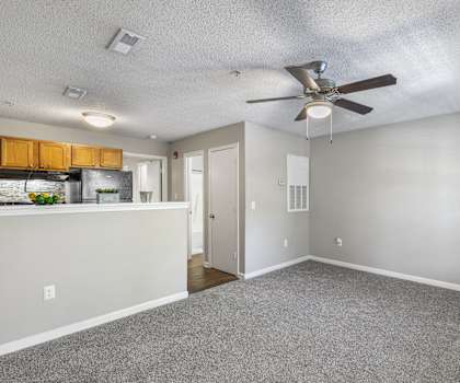 an empty living room with a ceiling fan and a kitchen