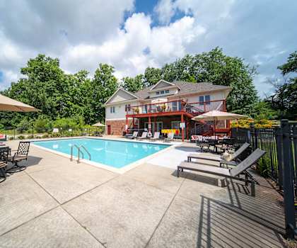 a swimming pool with chairs and umbrellas in front of a house