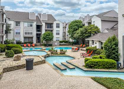 A swimming pool surrounded by apartment buildings and landscaping.