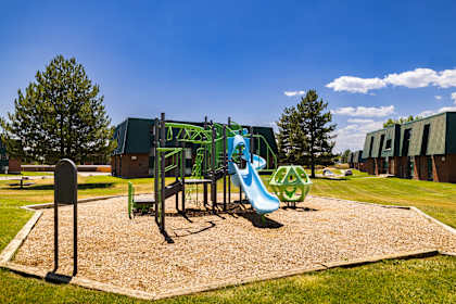 A playground with a green slide and a brown sandbox.