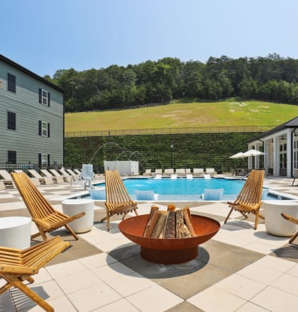 a pool with a fire pit and lounge chairs in front of a building with a grassy