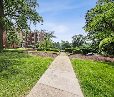 a sidewalk leading to an apartment building with grass and trees