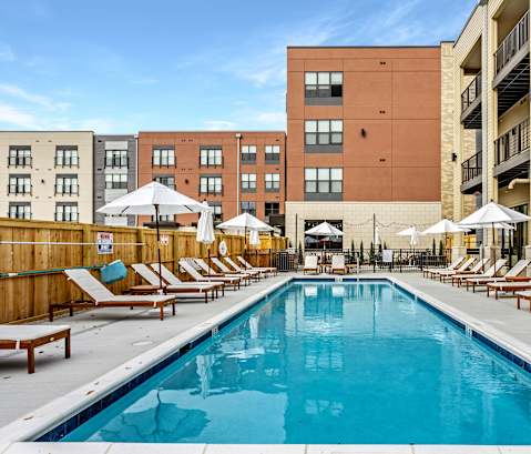 a swimming pool with chaise lounge chairs and umbrellas in front of a brick building