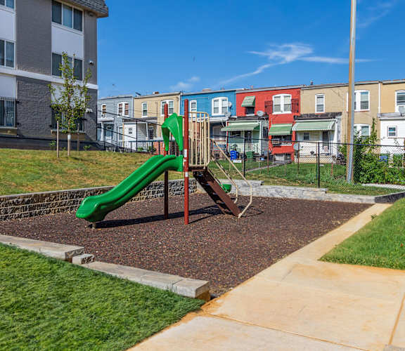 a playground with a green slide in front of an apartment building