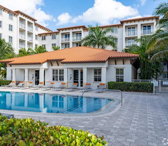A large white building with a red roof and a pool in front.