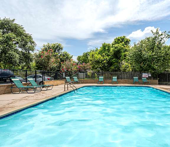 A large blue swimming pool surrounded by trees and lounge chairs.