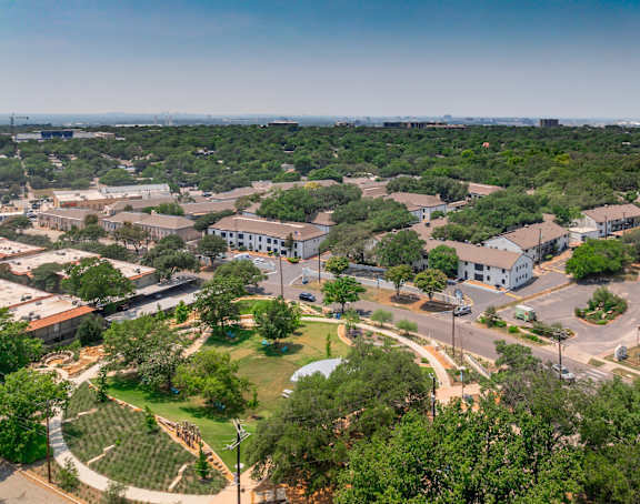 A bird's eye view of a residential area with houses, trees, and a clear sky.