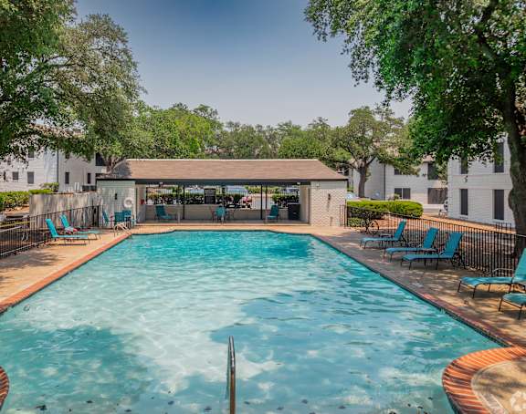 A large swimming pool surrounded by trees and chairs.