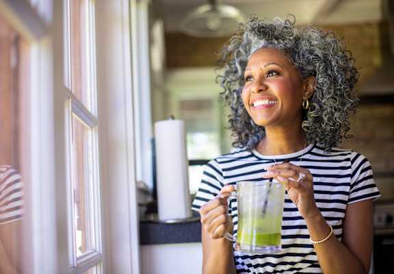 A woman with curly hair is holding a glass with a green drink in it.