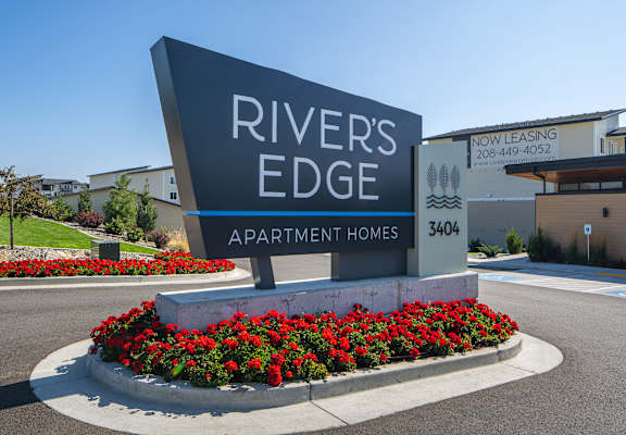 A sign for Rivers Edge Apartment Homes is surrounded by red flowers.