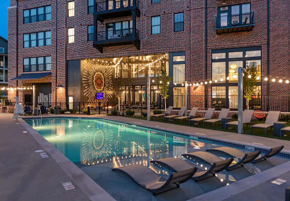 a pool area with lounge chairs and a building in the background at Livingston Flats Apartments, Chesterfield, VA, 23832