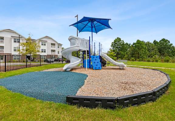A playground with a blue umbrella and a slide.