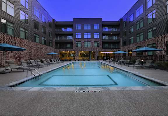 A swimming pool in a courtyard surrounded by chairs and umbrellas.
