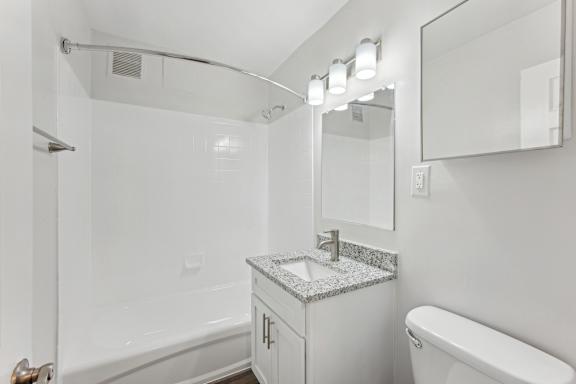 A white bathroom with a marble counter top and a white toilet.
