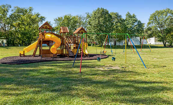 A playground with a yellow slide and a green swing set.