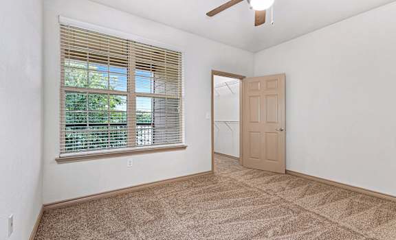 an empty living room with a large window and a ceiling fan