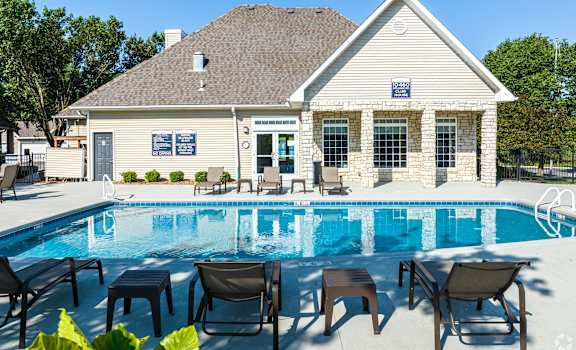 A poolside lounge area with chairs and tables is in front of a house.