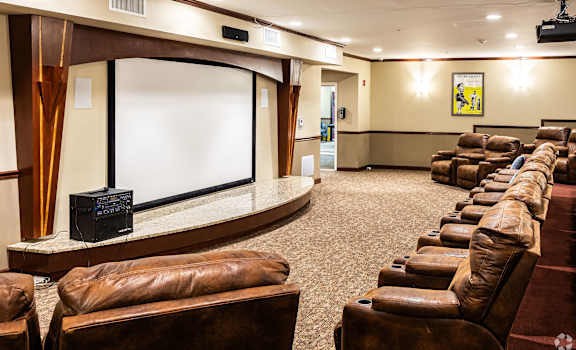 A row of brown leather chairs are arranged in front of a large screen.