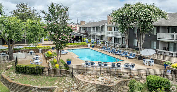 A pool surrounded by chairs and trees with a building in the background.
