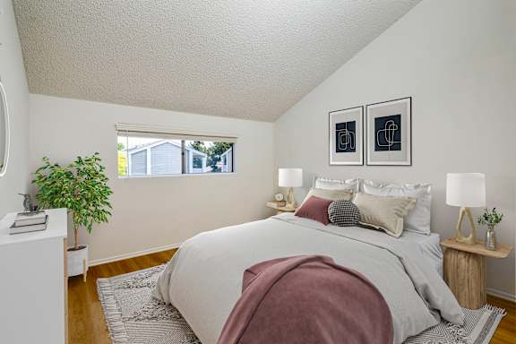 A bedroom with a bed, two lamps, and a potted plant.