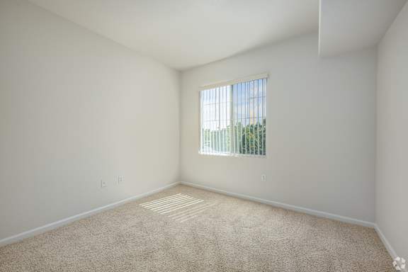 A room with a carpeted floor and a window with blinds.