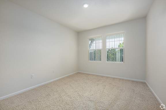 A room with a carpeted floor and a window with bars.
