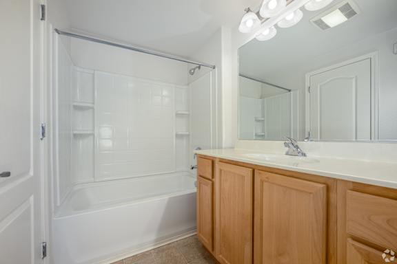 A white bathroom with wooden cabinets and a glass shower door.