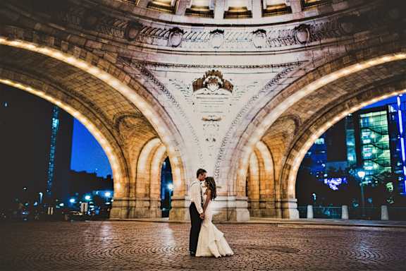 A couple in wedding attire stand under a beautifully lit archway. at The Pennsylvanian Apartments, Pittsburgh, Pennsylvania