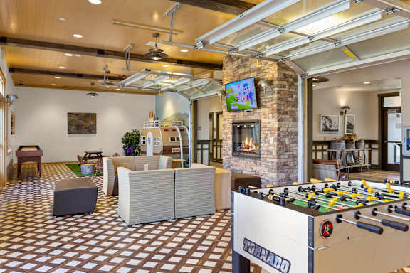 A foosball table is in the middle of a room with a brick wall and a TV.