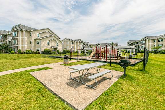 A picnic table sits in the middle of a concrete pad in a grassy area. at Stone Gate Apartments, North Carolina