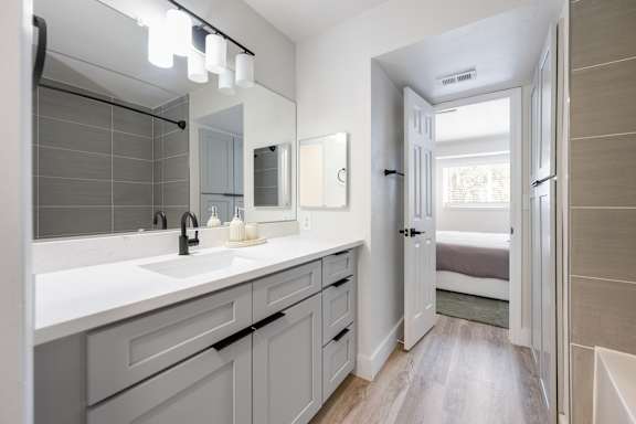 A bathroom with a sink, mirror, and a door leading to a bedroom.