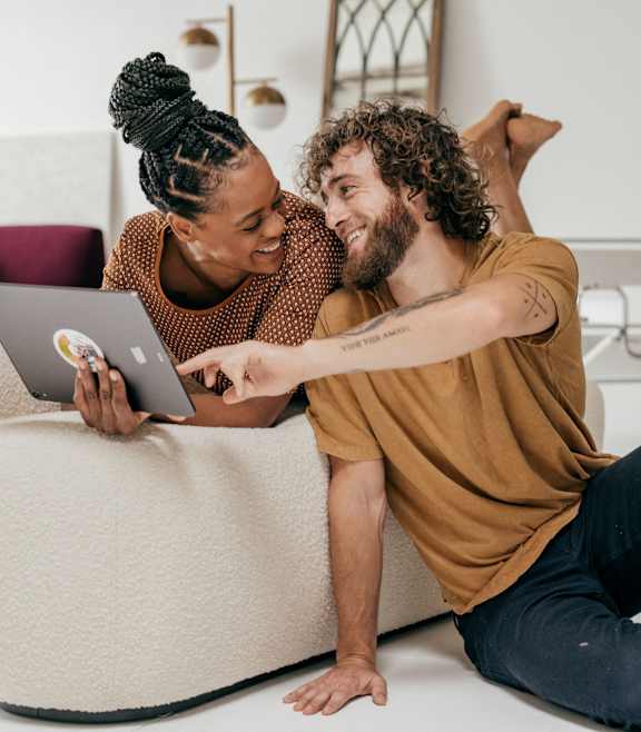 A man and woman are sitting on the floor in front of a laptop.