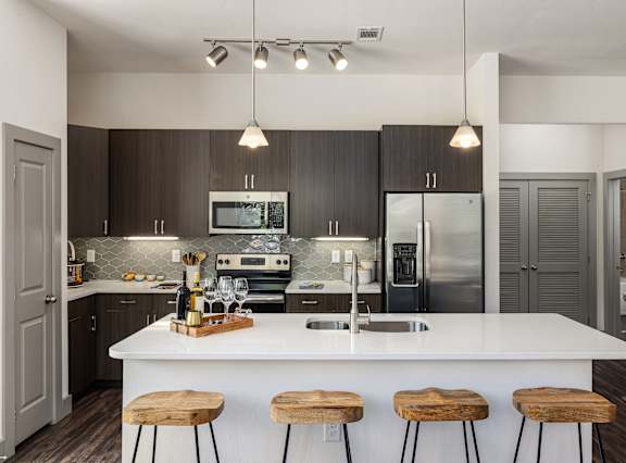 A modern kitchen with a white island and wooden stools.