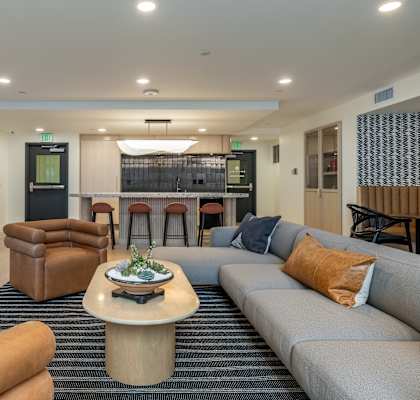 A modern living room with a grey sofa, a wooden coffee table, and a bar area in the background.