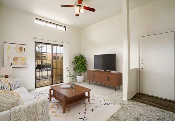 A living room with a white couch, a wooden coffee table, a flat screen TV, and a ceiling fan.