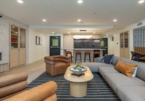 A modern living room with a grey sofa, a wooden coffee table, and a bar area in the background.