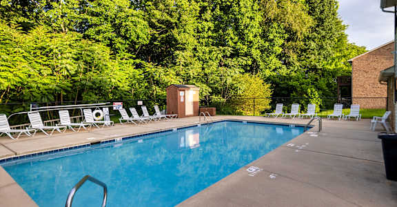 A pool surrounded by trees and chairs.