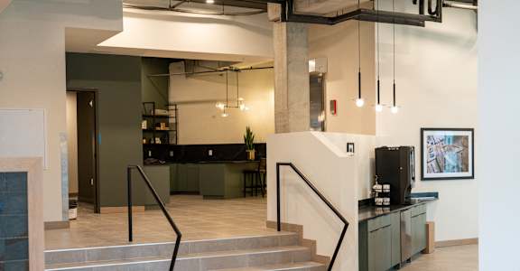 A staircase with a black handrail and grey steps leads to a kitchen area.