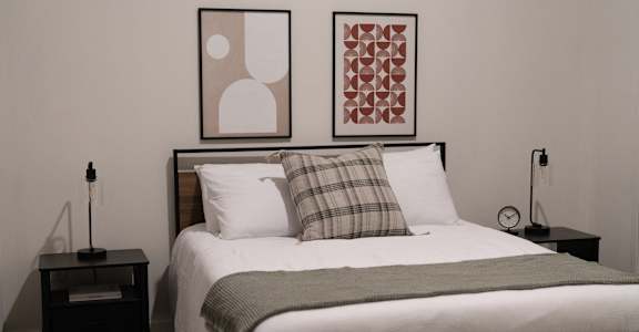 A bed with a white comforter and a green throw is flanked by two nightstands with lamps.