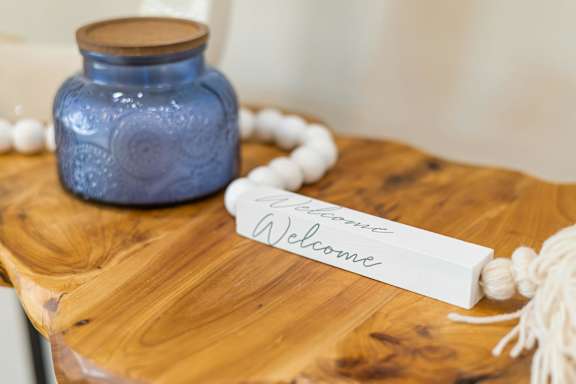 A blue jar sits on a wooden table next to a white sign that says "Welcome".