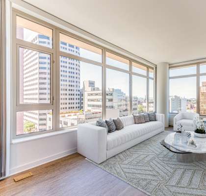 A living room with a large window overlooking a cityscape at The Grand Apartments, Oakland, CA, 94612