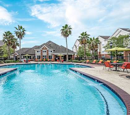 A large swimming pool in a residential area with red lounge chairs and umbrellas at The Fenwick Apartments, Humble, Texas