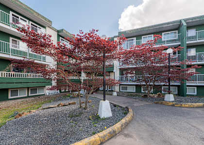 a view of the entrance to a green apartment building with red trees in front of it