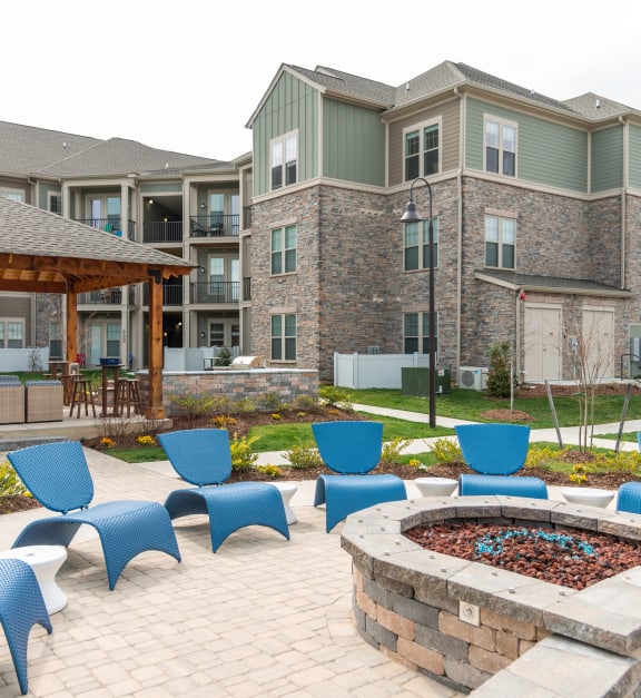 a fire pit with blue chairs and a pool in the background at Elan Williamsburg, Williamsburg, VA