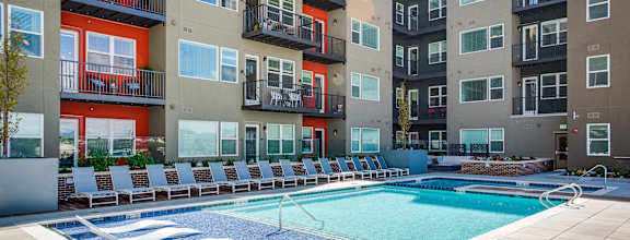 A swimming pool surrounded by lounge chairs in front of apartment buildings.